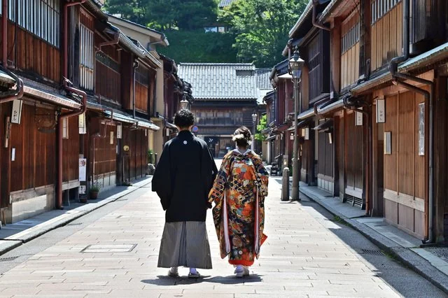 歴史ある町並みの石畳を並んで歩く、和装姿の男女の後ろ姿